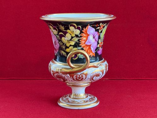 fig 1. A Regency Derby porcelain campana-shaped urn decorated with hand-painted pink roses on a black ground, featuring gilded handles and neoclassical lower gilding.