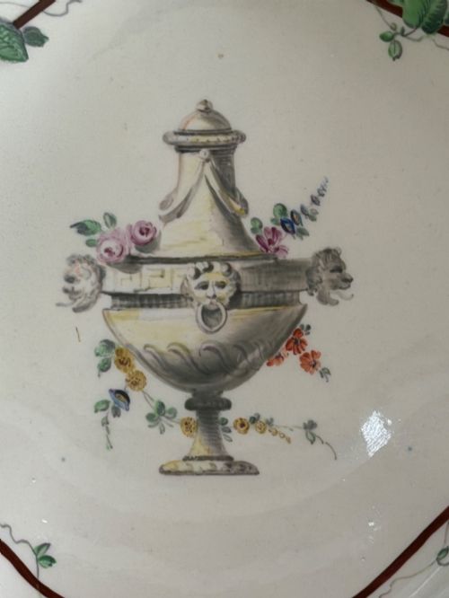 fig 1. An 18th-century shell-shaped white soft-paste porcelain dish decorated with a central classical urn motif, green leafy garland border, and gilded rim details.