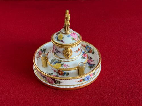 fig 1. A circular white porcelain inkstand featuring hand-painted floral decoration, gilt accents, pen holders, and a cover topped with a golden griffin finial.