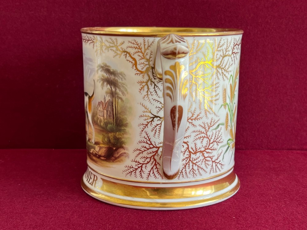 A Victorian English porcelain loving cup featuring two gilded scroll handles and a hand-painted hound named Drummer in a rural setting. View VI