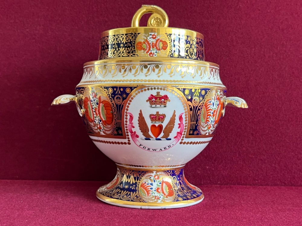 A Regency Chamberlain Worcester porcelain tureen decorated in an Imari style pattern of cobalt blue, iron red, and gilding, featuring a central crest with a heart and motto.