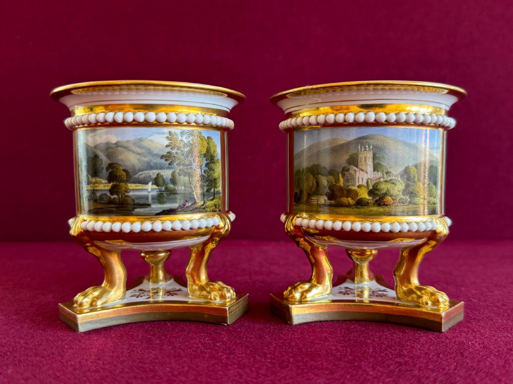 A pair of Regency Flight, Barr and Barr Worcester porcelain vases featuring hand-painted landscape scenes, gilded claw feet, and raised white bead mouldings.
