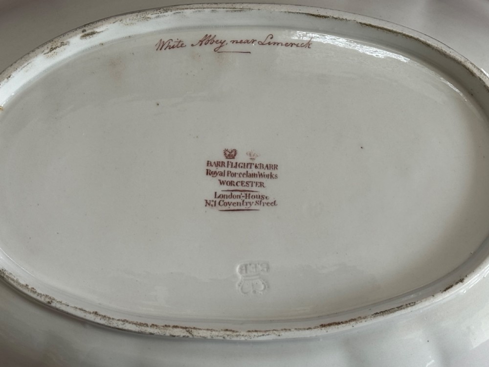 An oval Regency Worcester porcelain dessert dish featuring a hand-painted central river landscape with ruins, bordered by elaborate gold anthemion patterns over a pink background and a scalloped rim. View II