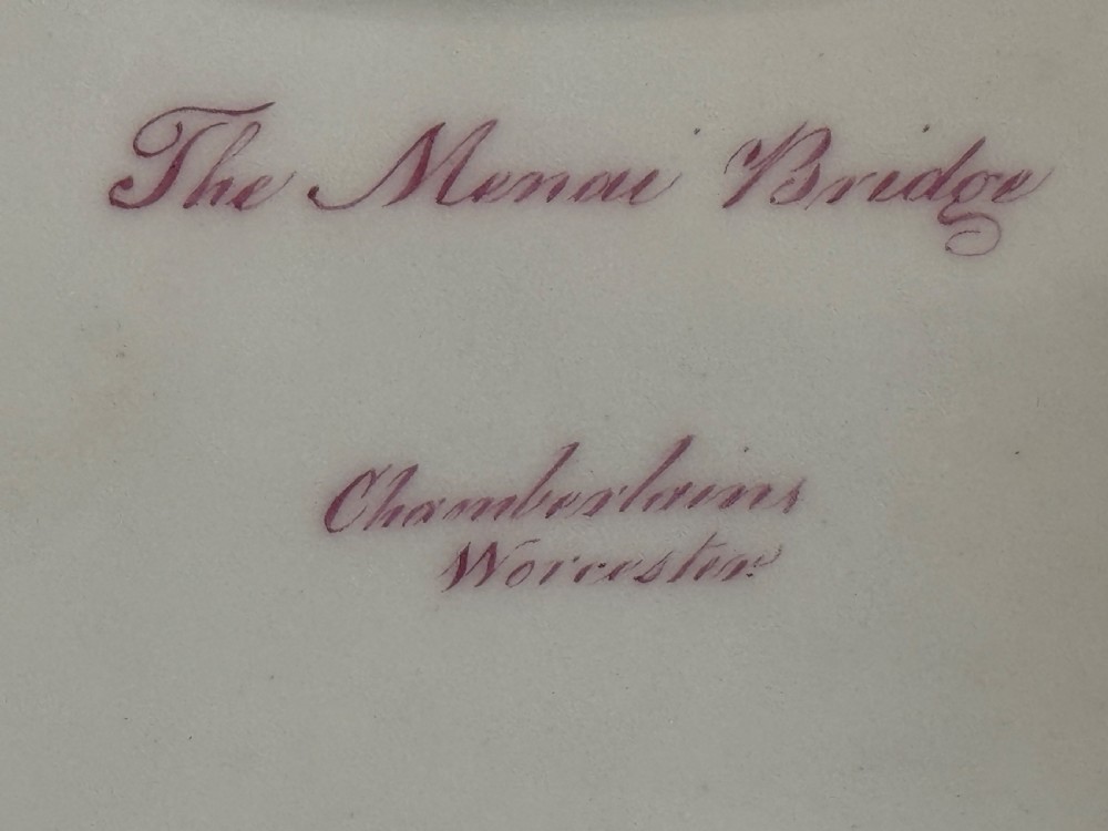 An antique rectangular porcelain basket with an overhead handle, decorated with three-dimensional applied shells along the rim and a hand-painted central view of the Menai Bridge on a cobalt blue dotted background. View V