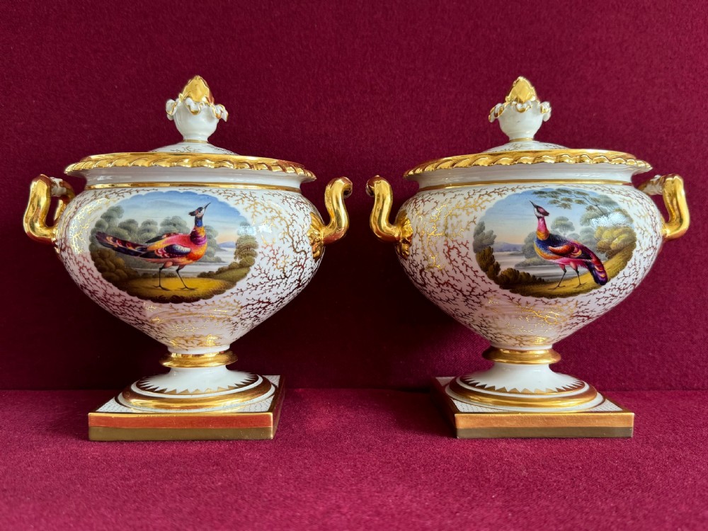 A pair of Regency Flight, Barr & Barr Worcester porcelain cream tureens featuring hand-painted bird panels, gilt seaweed pattern ornamentation, twin handles, and square plinth bases.