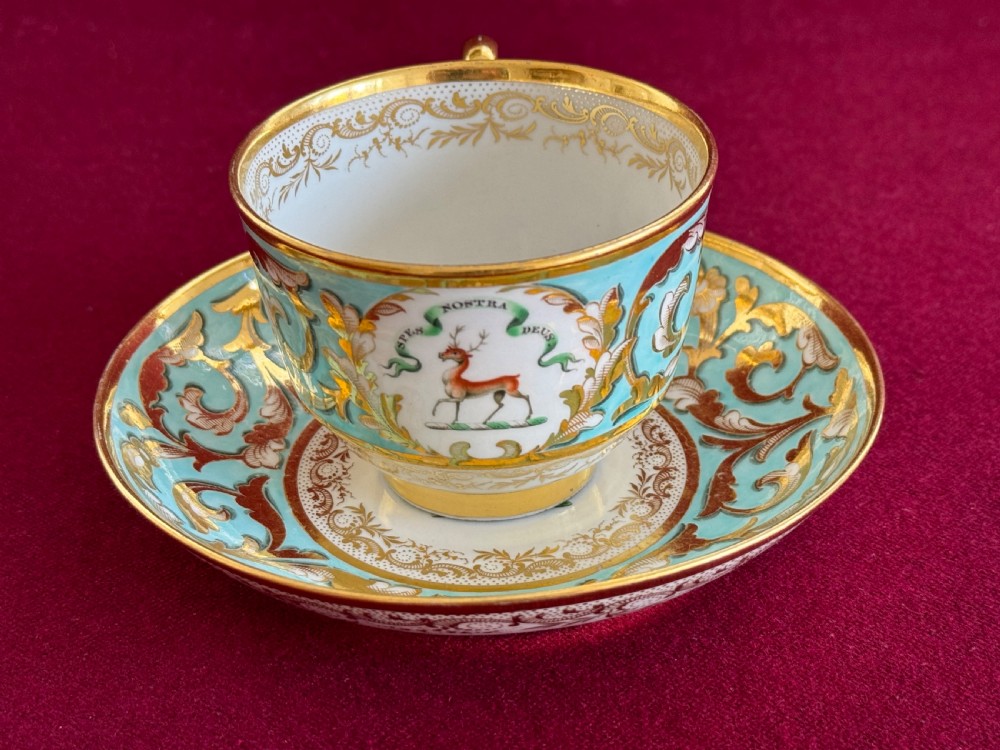 A Regency period Barr, Flight and Barr Worcester porcelain teacup and saucer featuring a turquoise ground, intricate gold gilding, and a heraldic family crest with a stag.