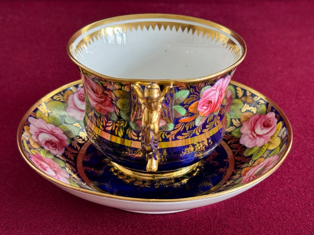 An antique Regency period Spode porcelain teacup and saucer featuring a cobalt blue background, hand-painted pink roses, gilded borders, and a gilded figural handle. View IV