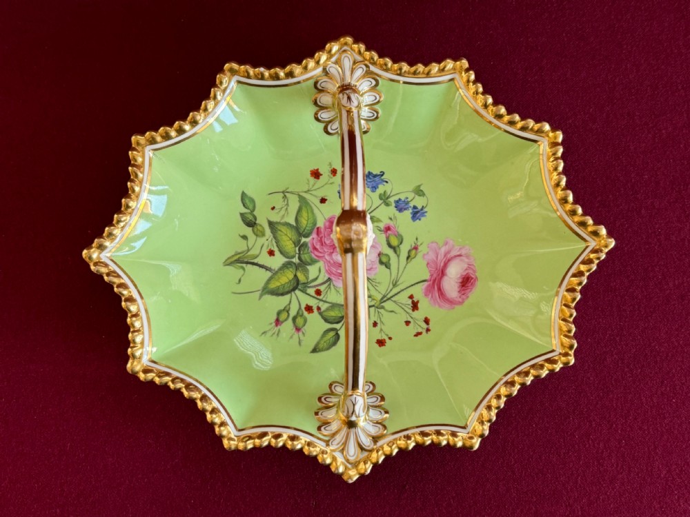 An antique Flight, Barr & Barr Worcester porcelain dessert basket featuring an apple green ground with central hand-painted roses, an overhead handle, and a lobed gilt gadrooned border.