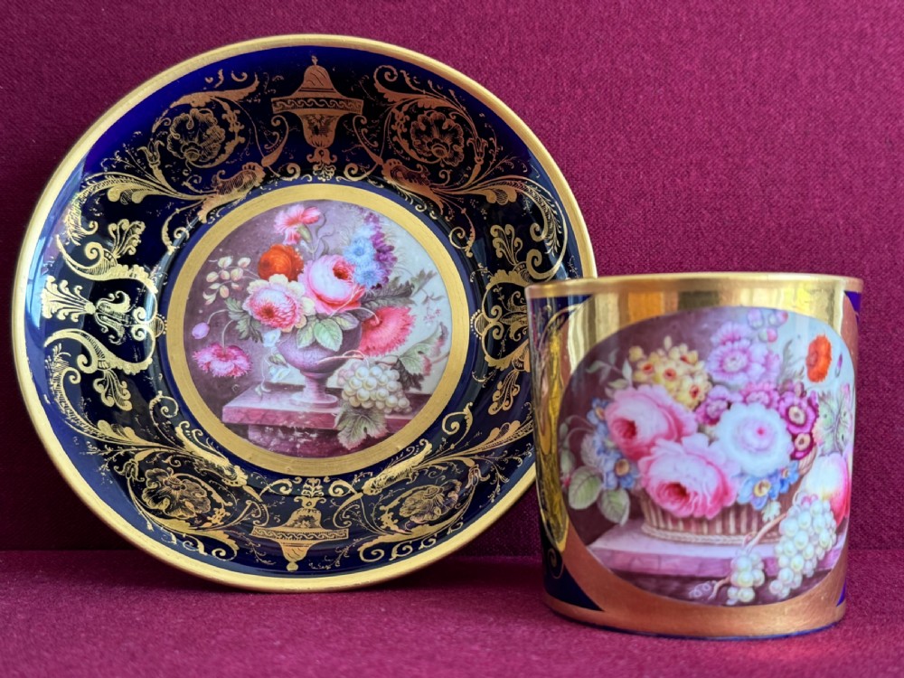 A cobalt blue and gilded Minton porcelain coffee can and matching saucer decorated with hand-painted floral still-life panels.