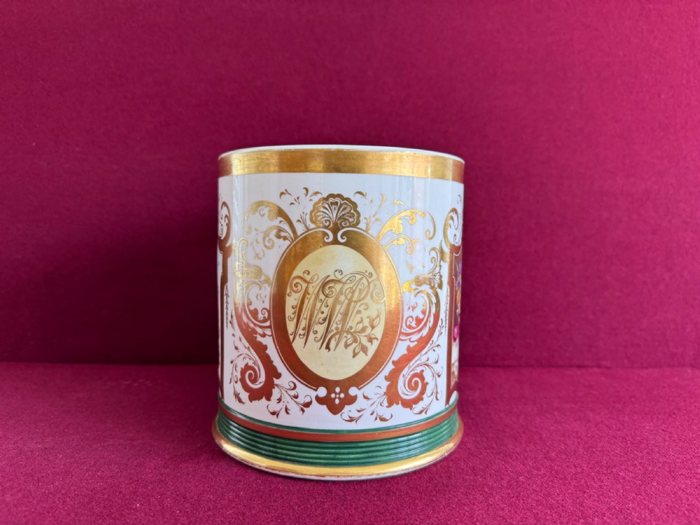 A cylindrical porcelain porter mug decorated with gold leaf scrollwork, a green reeded base, and a hand-painted floral still life panel. View II