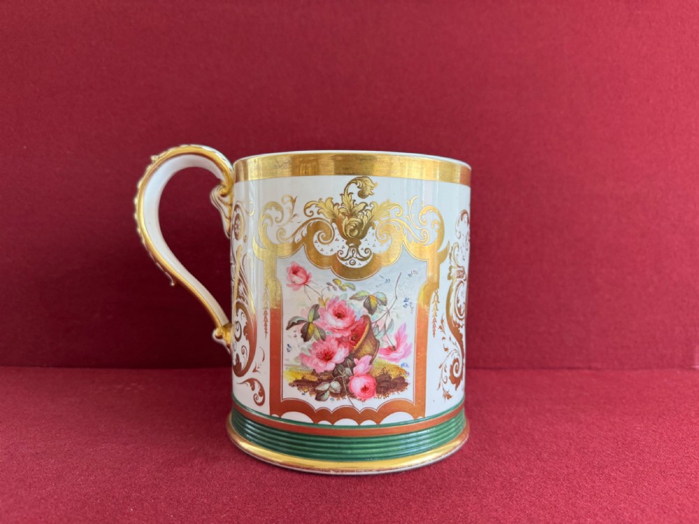 A cylindrical porcelain porter mug decorated with gold leaf scrollwork, a green reeded base, and a hand-painted floral still life panel. View III