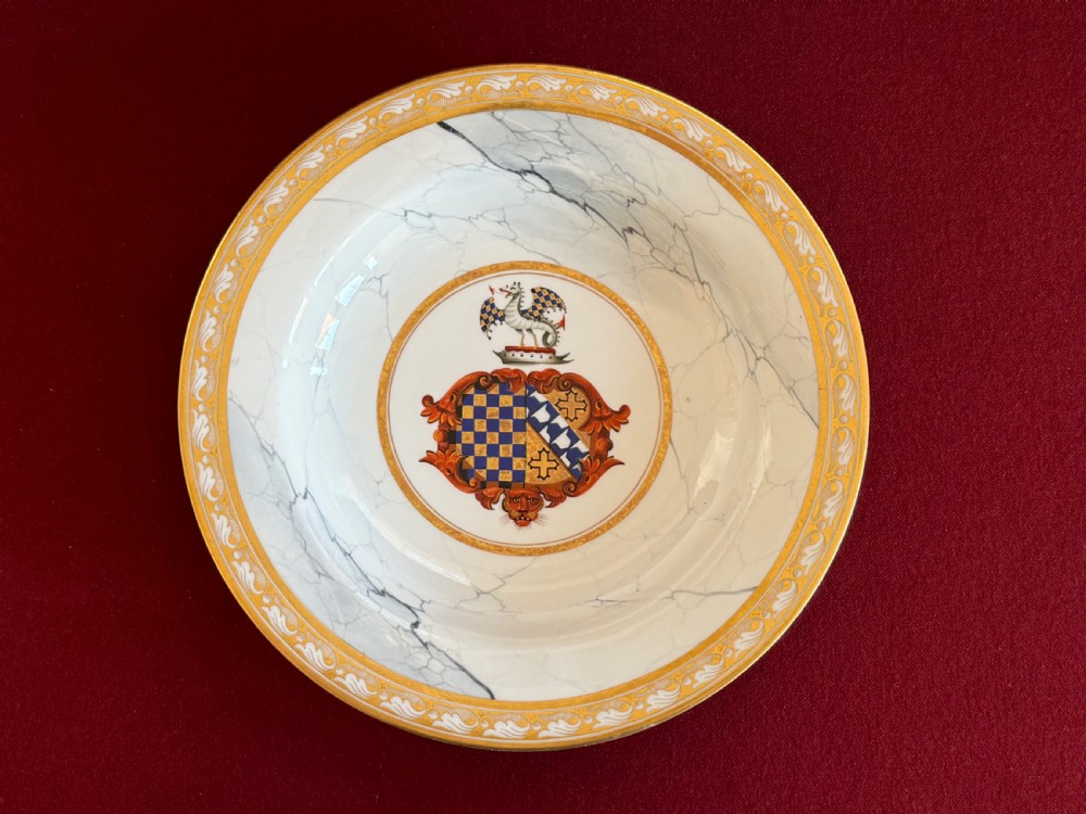 An antique circular porcelain soup plate featuring a central heraldic coat of arms, a faux marble pattern on the rim, and decorative gilded borders.