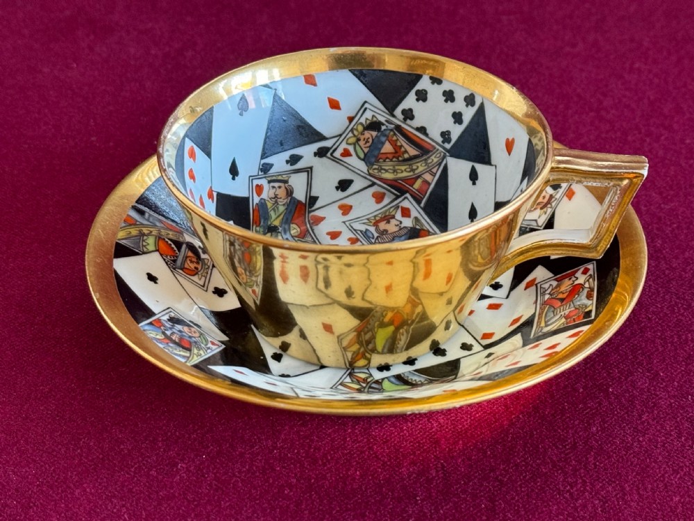 An antique Regency period porcelain teacup and matching saucer featuring a hand-painted playing card motif on the interior and a gilded exterior finish.