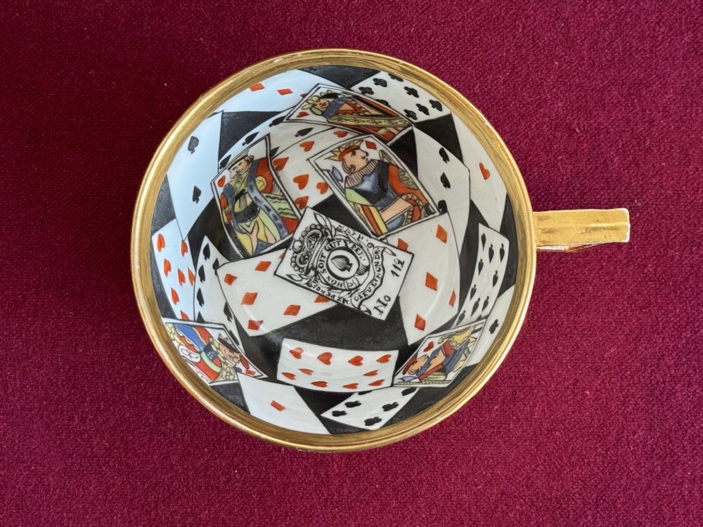 An antique Regency period porcelain teacup and matching saucer featuring a hand-painted playing card motif on the interior and a gilded exterior finish. View VII