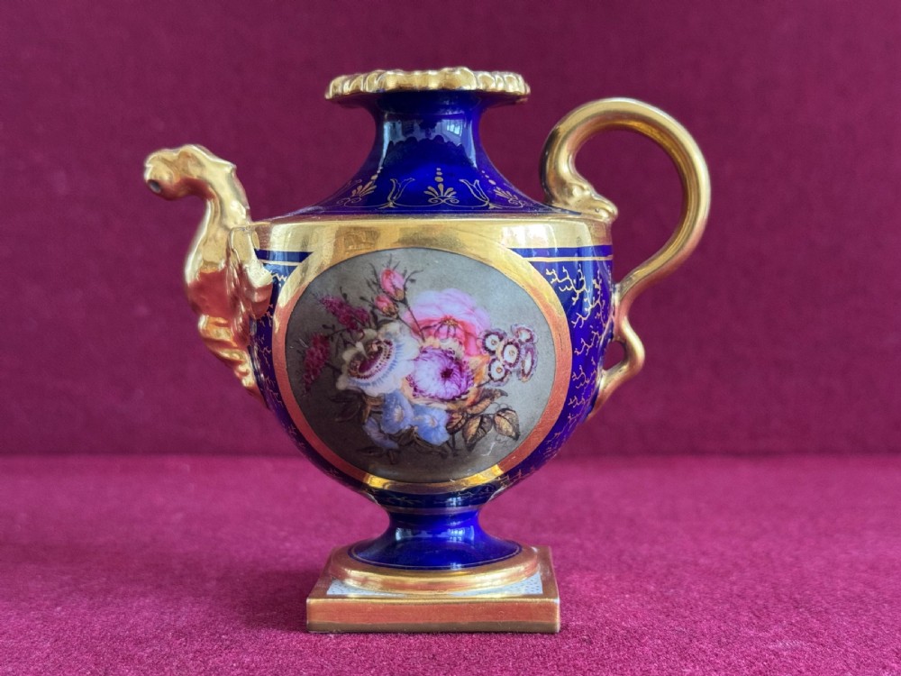 A Regency era Flight, Barr and Barr Worcester cobalt blue porcelain rose water sprinkler decorated with a hand-painted floral cartouche and gilt accents on a square base.