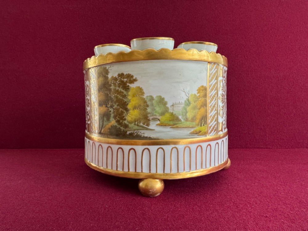 An antique Regency porcelain bough pot featuring a hand-painted landscape scene framed by gold leaf decoration and raised on ball feet.