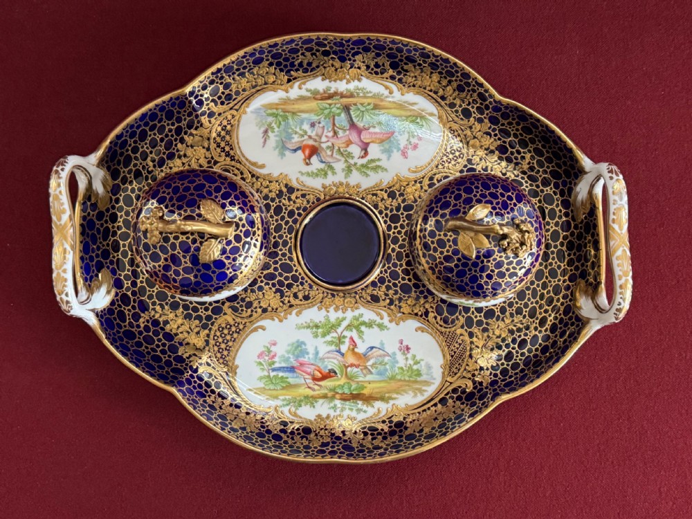 An oval cobalt blue porcelain inkstand featuring twin handles, extensive gold gilding, two lidded pots, and central hand-painted reserve panels displaying birds.