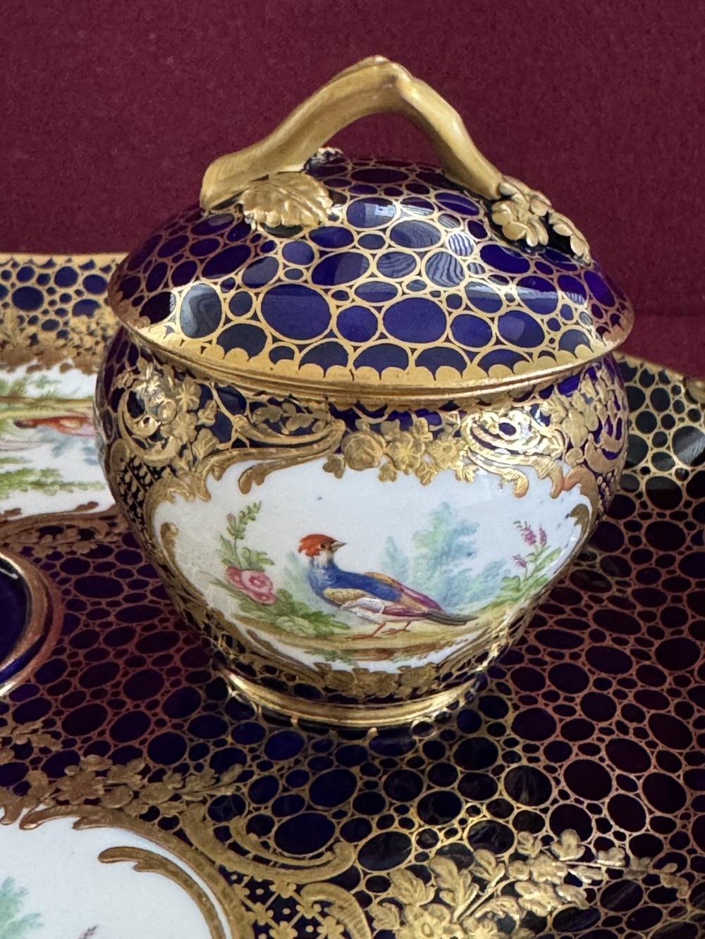 An oval cobalt blue porcelain inkstand featuring twin handles, extensive gold gilding, two lidded pots, and central hand-painted reserve panels displaying birds. View III