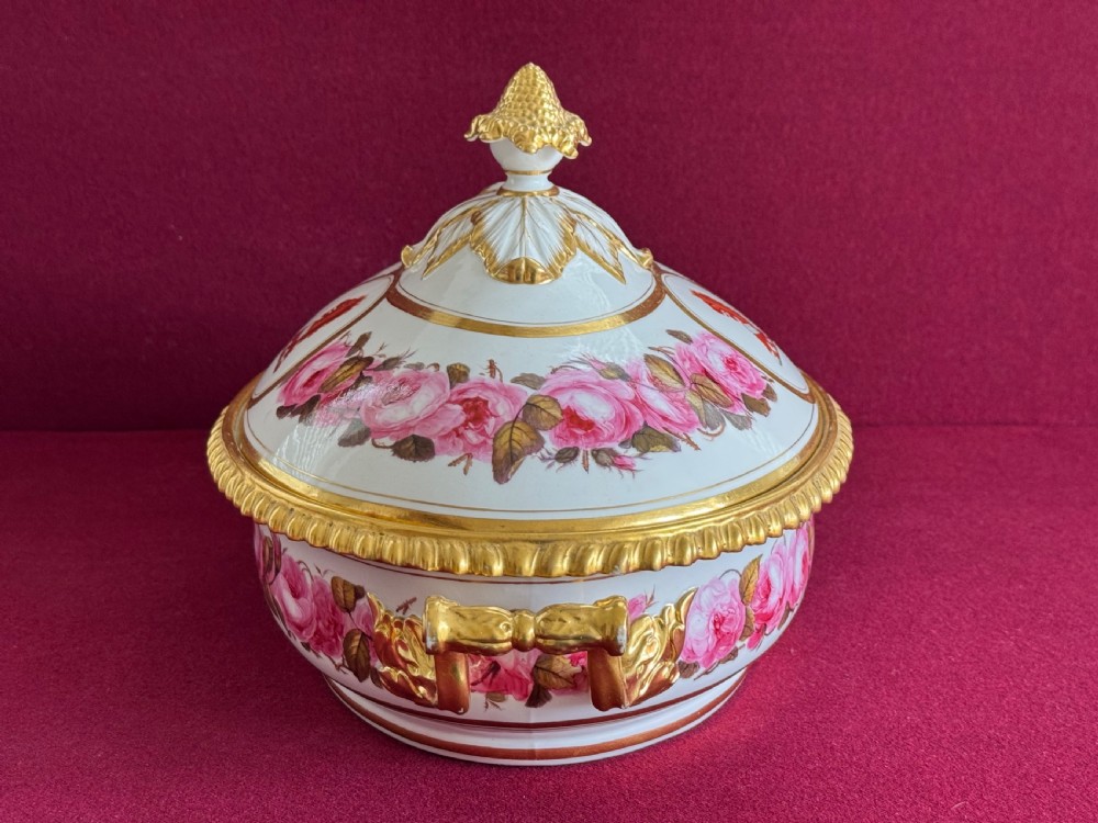 An oval Regency Worcester porcelain entree dish with a fitted lid, featuring hand-painted pink rose garlands, gilt gadrooned rims, twin gilded handles, a heraldic lion crest, and a gold leaf-and-pineapple finial. View II