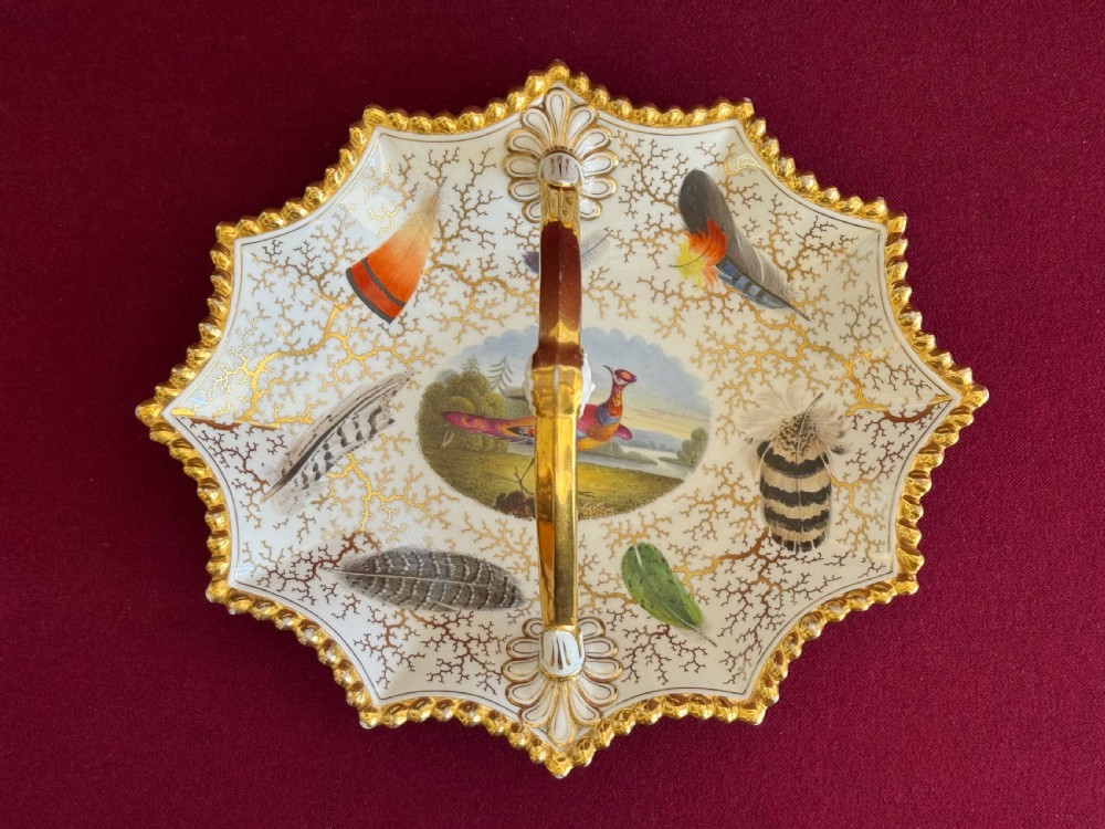 A Regency Flight, Barr and Barr Worcester porcelain basket featuring hand-painted feathers, a central landscape with a bird, and gold seaweed gilding on a white background with a central handle.