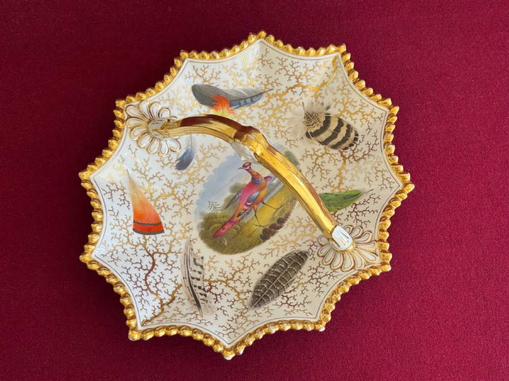 A Regency Flight, Barr and Barr Worcester porcelain basket featuring hand-painted feathers, a central landscape with a bird, and gold seaweed gilding on a white background with a central handle. View II