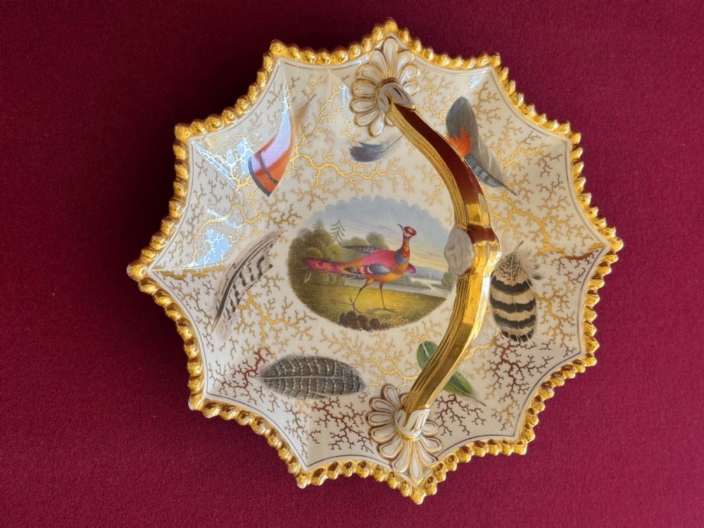 A Regency Flight, Barr and Barr Worcester porcelain basket featuring hand-painted feathers, a central landscape with a bird, and gold seaweed gilding on a white background with a central handle. View V