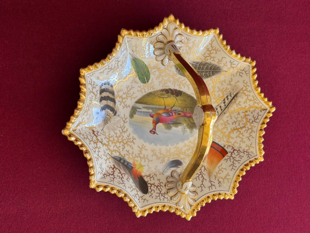 A Regency Flight, Barr and Barr Worcester porcelain basket featuring hand-painted feathers, a central landscape with a bird, and gold seaweed gilding on a white background with a central handle. View VI
