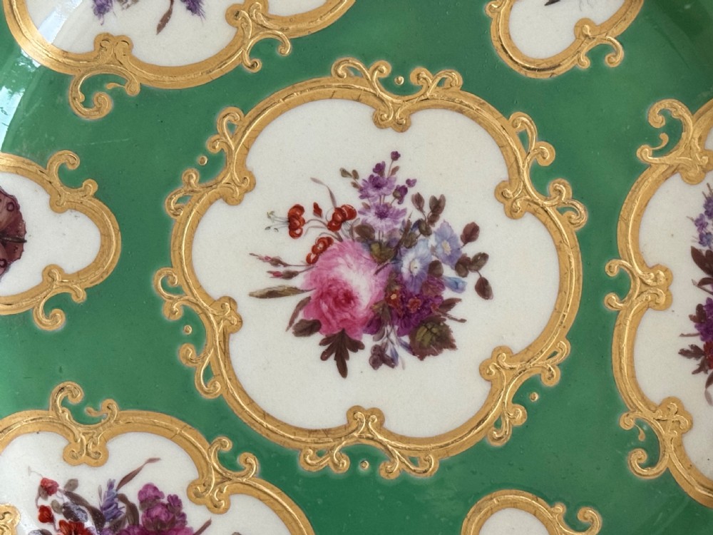 A circular green porcelain plate featuring hand-painted floral cartouches surrounded by gilded rococo scrollwork and central floral and butterfly vignettes. View III