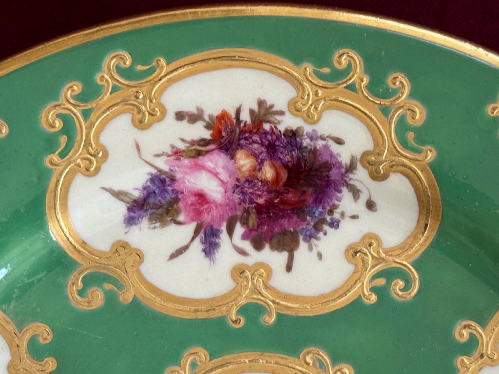 A circular green porcelain plate featuring hand-painted floral cartouches surrounded by gilded rococo scrollwork and central floral and butterfly vignettes. View IV