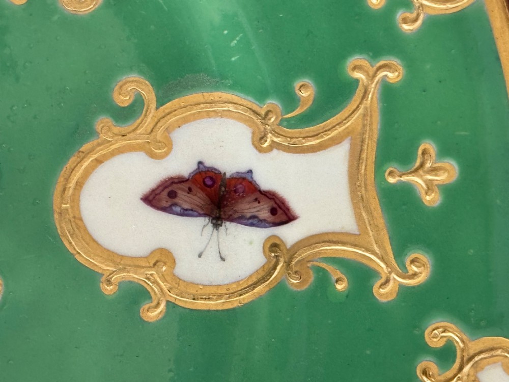 A circular green porcelain plate featuring hand-painted floral cartouches surrounded by gilded rococo scrollwork and central floral and butterfly vignettes. View VII
