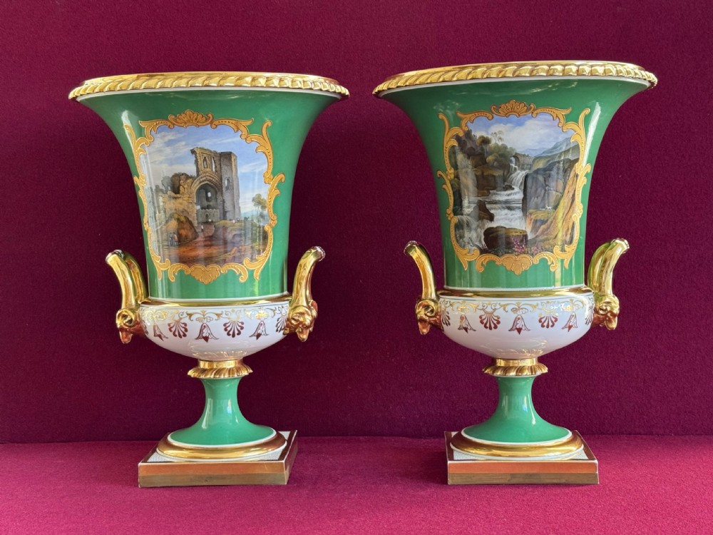 A pair of Regency porcelain urn vases featuring apple green grounds, gilt goat-head handles, and central hand-painted landscape scenes.