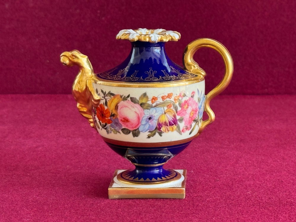 A Regency Flight, Barr and Barr Worcester porcelain rose water sprinkler featuring a cobalt blue ground, hand-painted floral band, zoomorphic gilded spout, and loop handle on a square pedestal base.