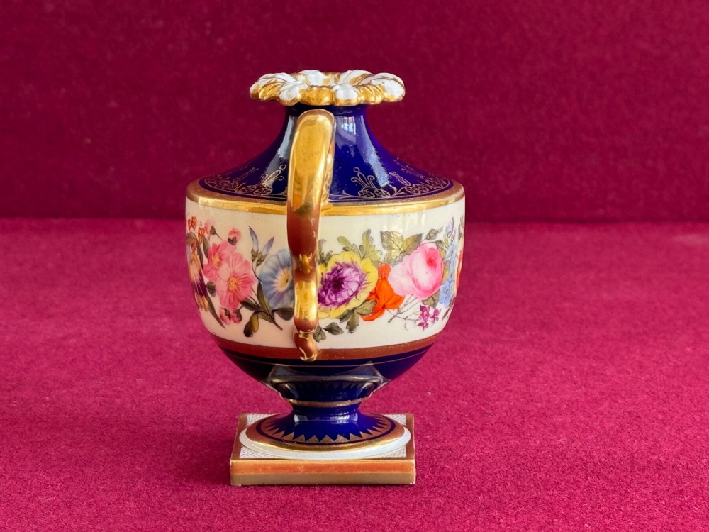 A Regency Flight, Barr and Barr Worcester porcelain rose water sprinkler featuring a cobalt blue ground, hand-painted floral band, zoomorphic gilded spout, and loop handle on a square pedestal base. View III
