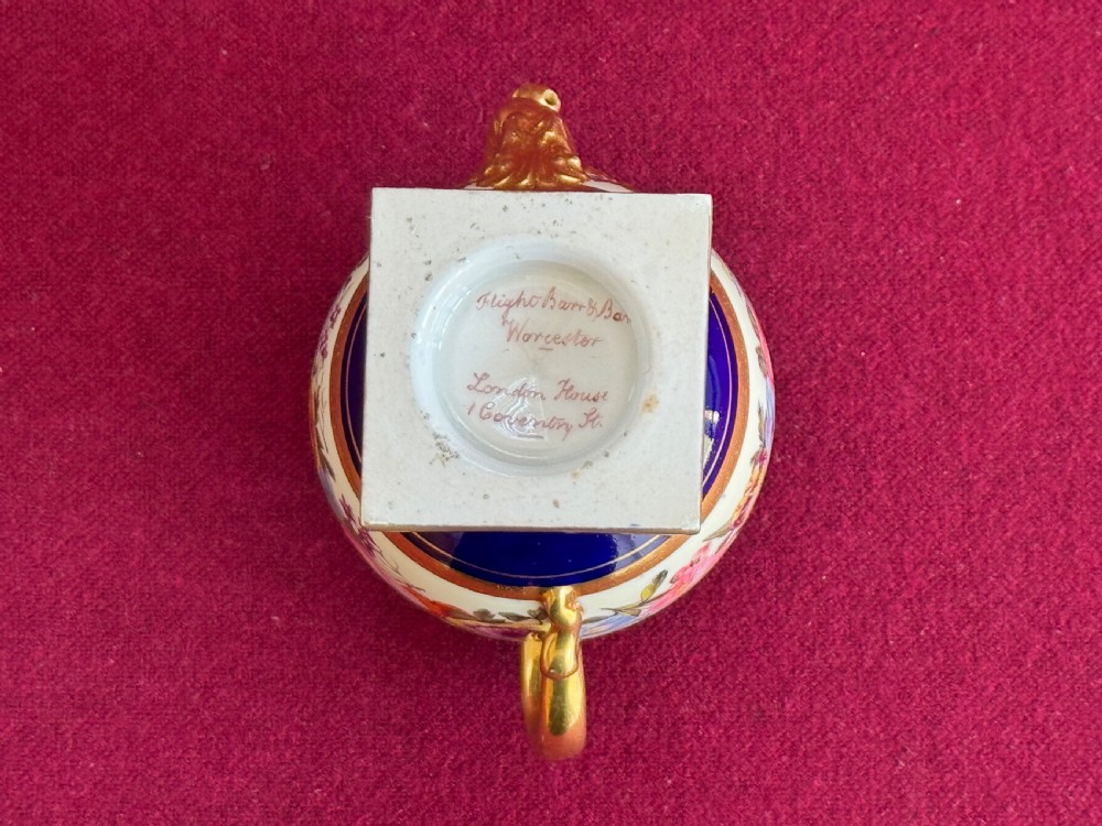 A Regency Flight, Barr and Barr Worcester porcelain rose water sprinkler featuring a cobalt blue ground, hand-painted floral band, zoomorphic gilded spout, and loop handle on a square pedestal base. View V