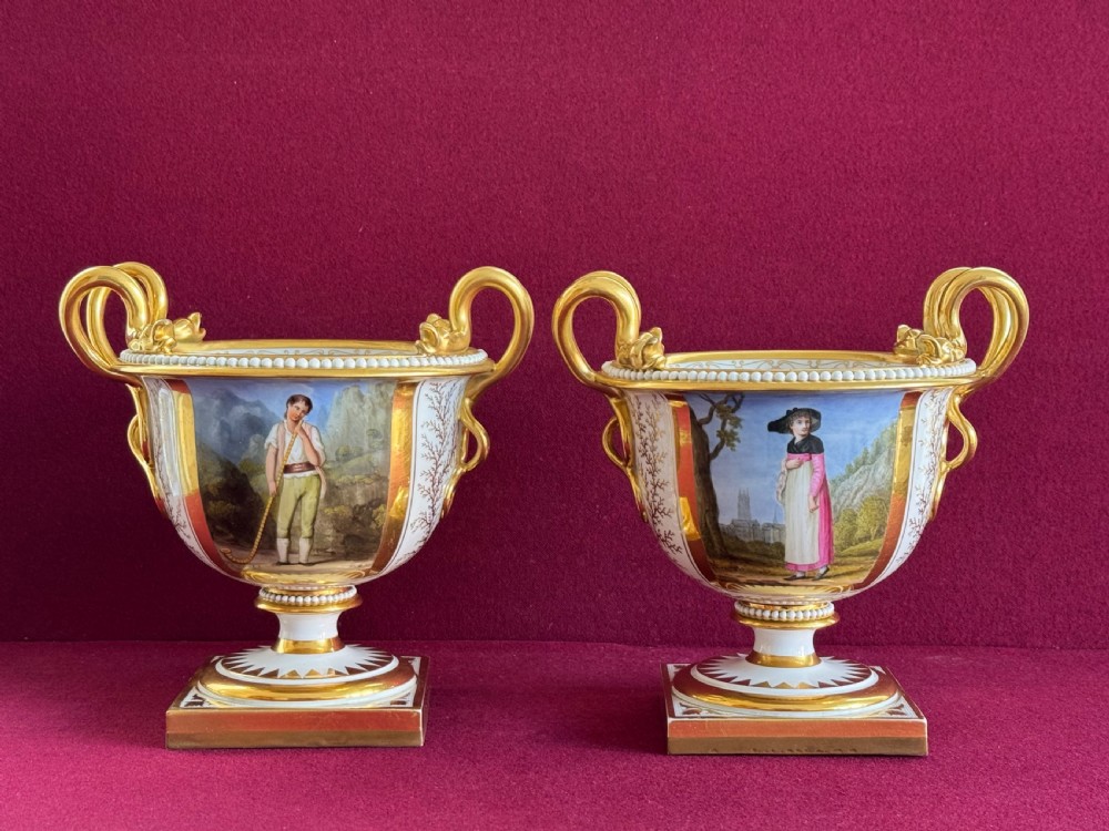 A pair of Regency Flight, Barr and Barr Worcester porcelain urn-shaped vases featuring hand-painted figurative panels, gilded scroll handles, beaded rims, and square plinth bases.