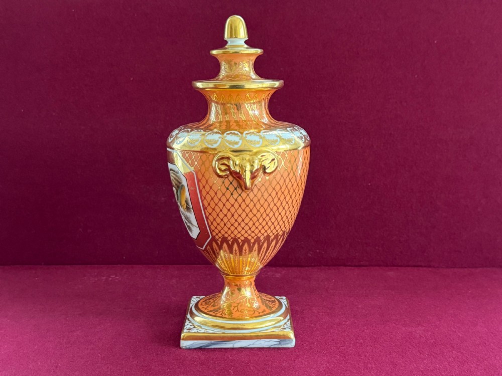 A Regency Chamberlain Worcester porcelain urn-shaped vase with a lid, featuring an orange pattern ground, gilded accents, side mask handles, and a painted feather panel on a square base. View II