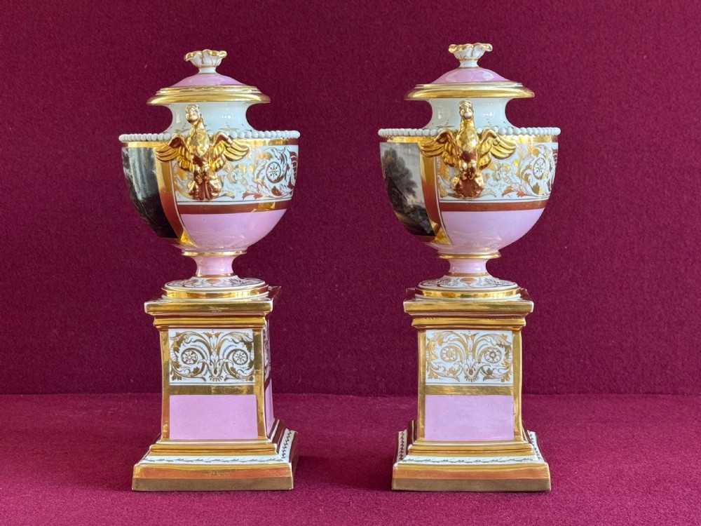 A three-piece Flight, Barr and Barr Worcester porcelain garniture set with hand-painted landscape scenes, pink ground borders, and gilded scroll handles resting on square pedestal bases. View XII