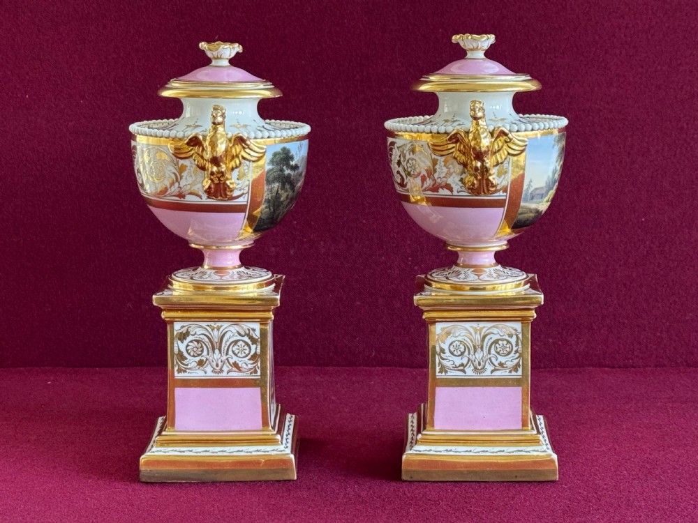 A three-piece Flight, Barr and Barr Worcester porcelain garniture set with hand-painted landscape scenes, pink ground borders, and gilded scroll handles resting on square pedestal bases. View XIV