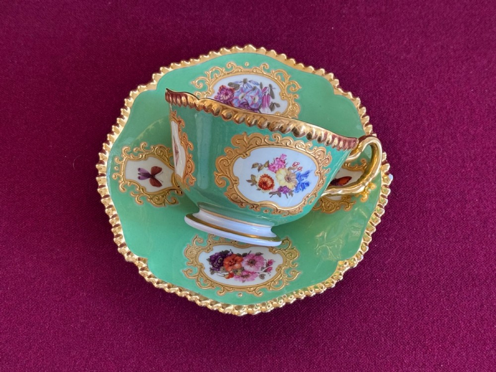 An antique Flight, Barr & Barr porcelain teacup and saucer featuring an apple green ground, hand-painted floral panels, and gilt gadrooned rims.
