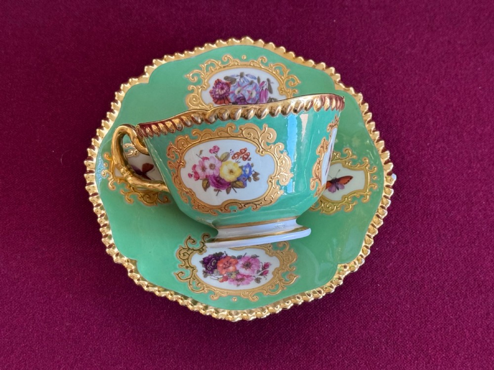 An antique Flight, Barr & Barr porcelain teacup and saucer featuring an apple green ground, hand-painted floral panels, and gilt gadrooned rims. View II