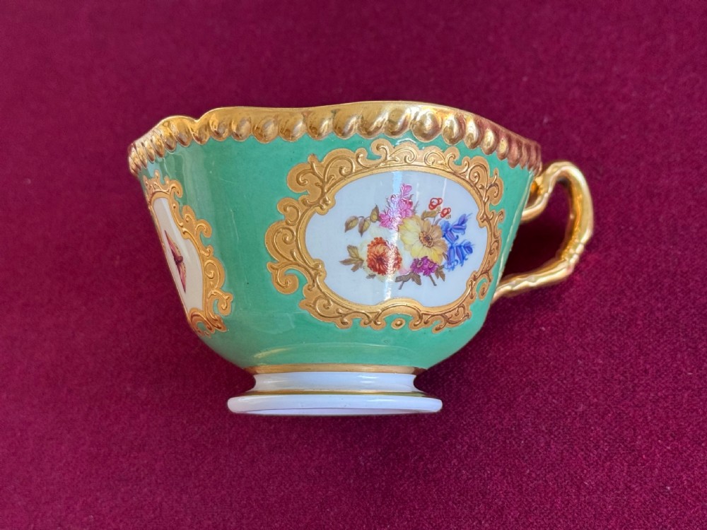 An antique Flight, Barr & Barr porcelain teacup and saucer featuring an apple green ground, hand-painted floral panels, and gilt gadrooned rims. View IV