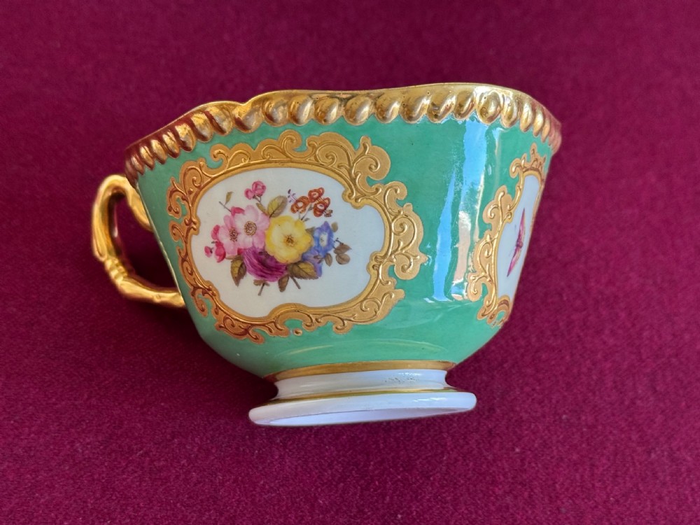 An antique Flight, Barr & Barr porcelain teacup and saucer featuring an apple green ground, hand-painted floral panels, and gilt gadrooned rims. View VI