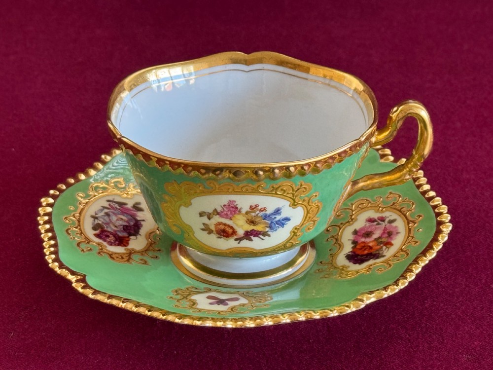 An antique Flight, Barr & Barr porcelain teacup and saucer featuring an apple green ground, hand-painted floral panels, and gilt gadrooned rims. View VII