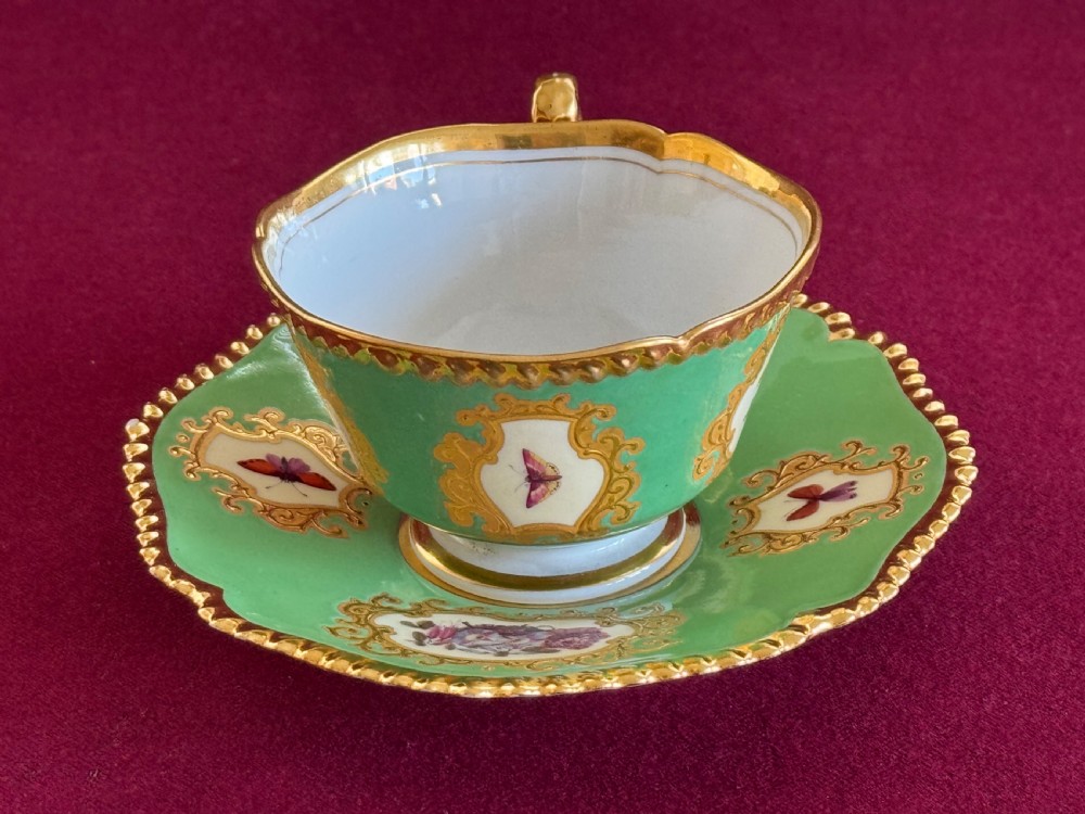 An antique Flight, Barr & Barr porcelain teacup and saucer featuring an apple green ground, hand-painted floral panels, and gilt gadrooned rims. View VIII