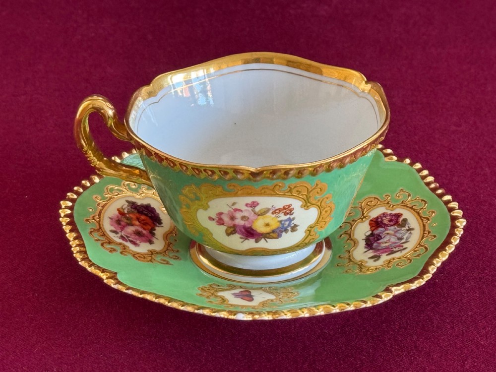 An antique Flight, Barr & Barr porcelain teacup and saucer featuring an apple green ground, hand-painted floral panels, and gilt gadrooned rims. View IX