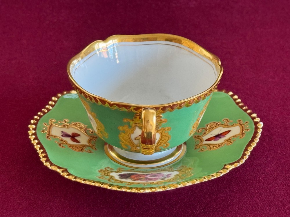 An antique Flight, Barr & Barr porcelain teacup and saucer featuring an apple green ground, hand-painted floral panels, and gilt gadrooned rims. View X