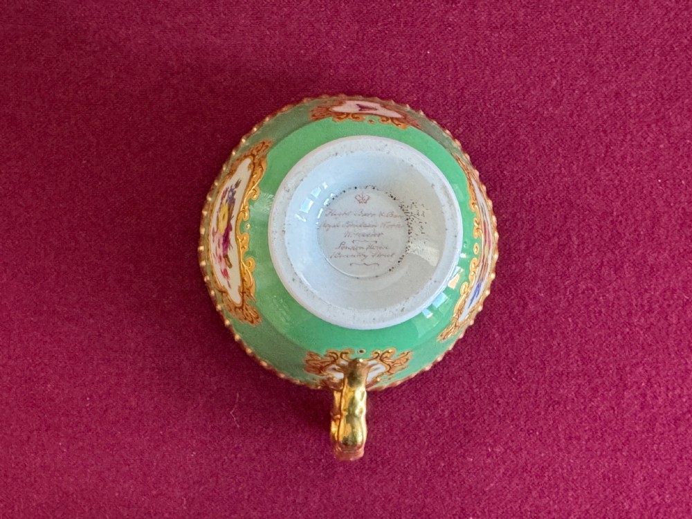 An antique Flight, Barr & Barr porcelain teacup and saucer featuring an apple green ground, hand-painted floral panels, and gilt gadrooned rims. View XII