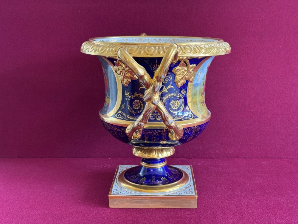 A Regency Flight, Barr and Barr Worcester cobalt blue porcelain Warwick urn featuring twin gilt vine-twisted handles, intricate gilt tooling, and a central hand-painted panel depicting two figures in a landscape. View IV