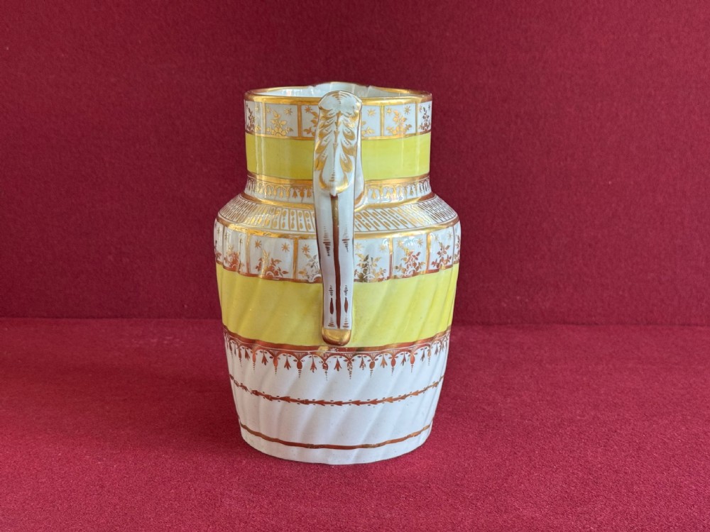 A white and yellow antique porcelain jug decorated with gilt detailing, spiral fluting, and a central armorial crest featuring a painted lion. View II