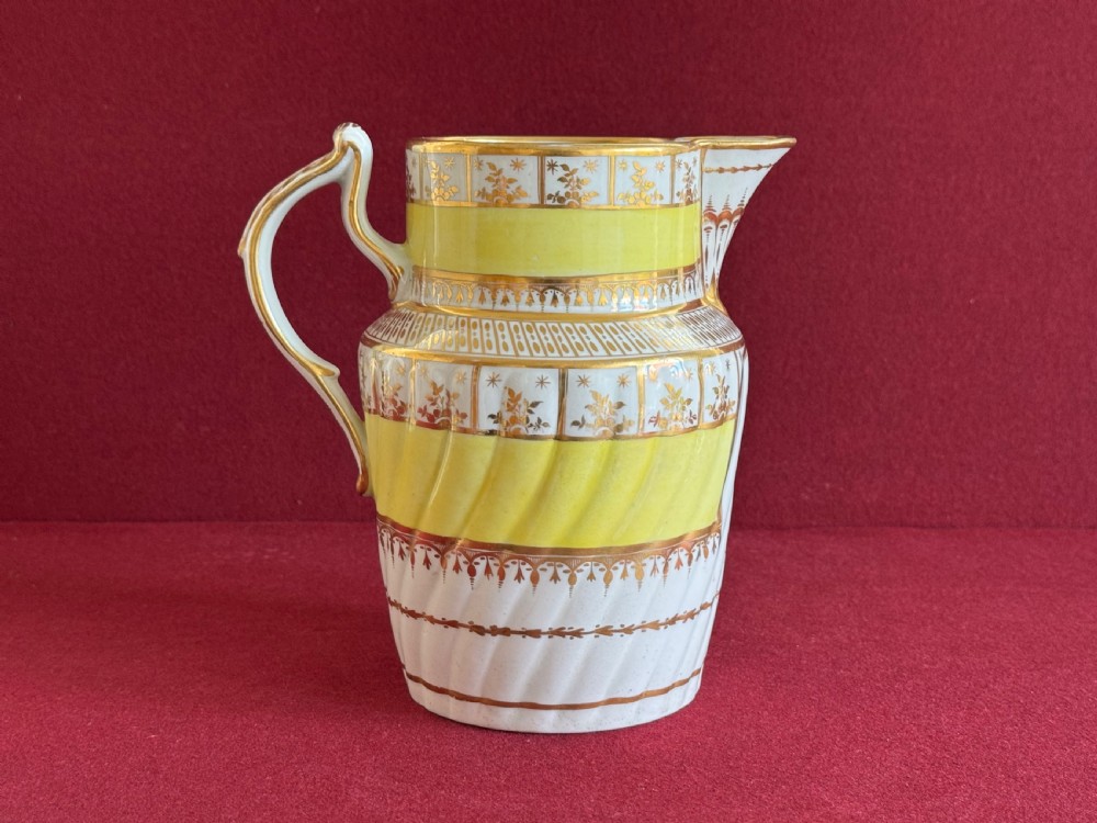 A white and yellow antique porcelain jug decorated with gilt detailing, spiral fluting, and a central armorial crest featuring a painted lion. View III